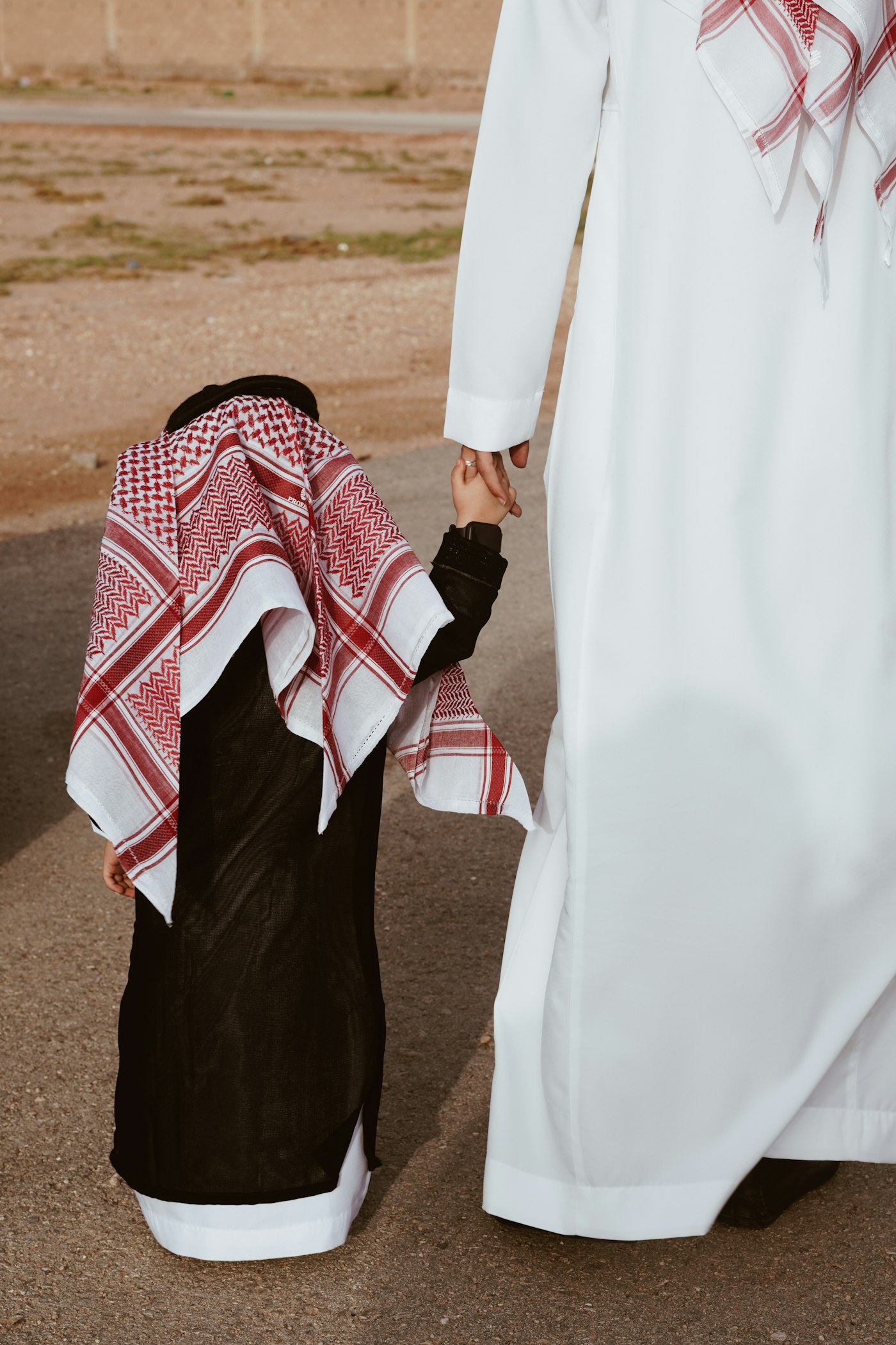 أب بثوب وشماغ يمسك يد طفله أثناء المشي